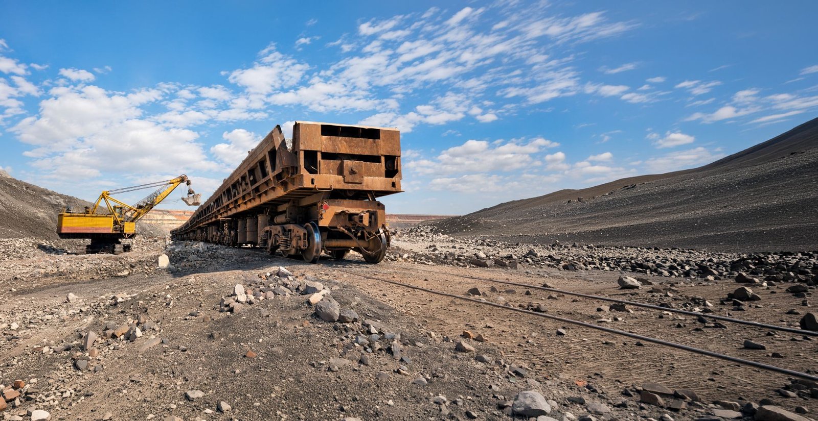 Vagão ferroviário em área de mineração com escavadeira ao fundo
